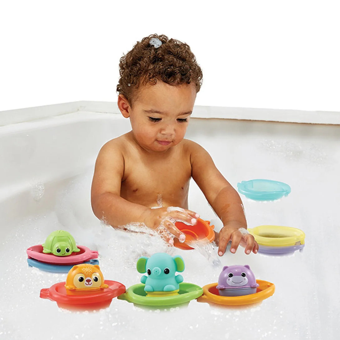 Toddler sitting in a bath tub, surrounded by bubbles, and playing with the VTech Stack & Splash Bathtime Boats bath toy set.