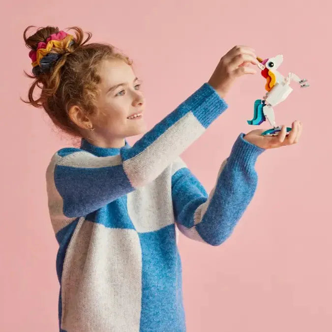 A young girl holds LEGO 31140 Magical Unicorn up in her left hand, while using her right hand to adjust the model's pose.