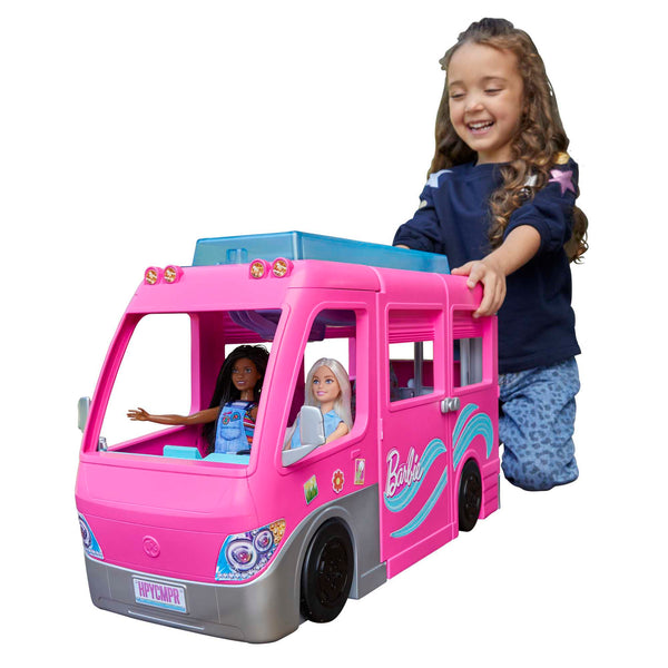 Child playing with a pink Barbie camper van featuring dolls inside on a white background